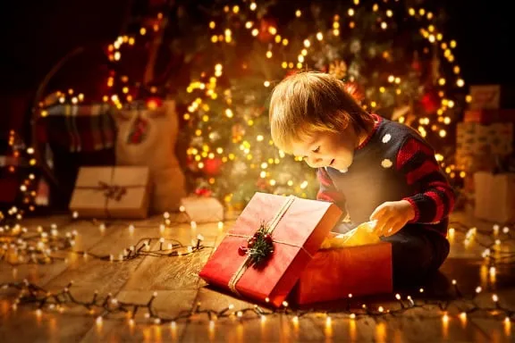 Chłopiec otwiera świąteczny prezent pod choinką