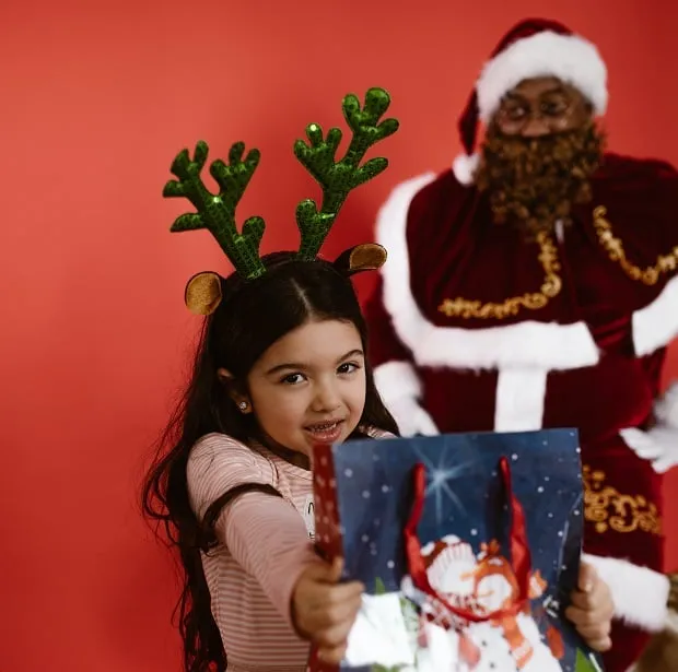 Dziewczyna trzyma torebkę z prezentem, w tle Mikołaj