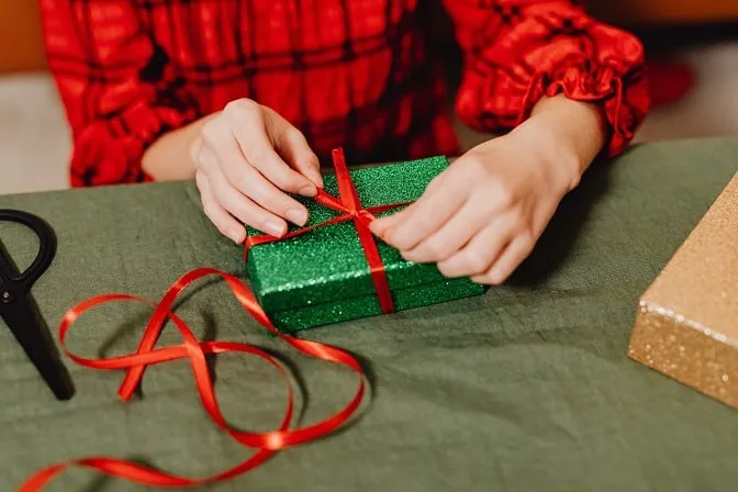 Kobieta pakuje prezent w zielone pudełko ozdobne