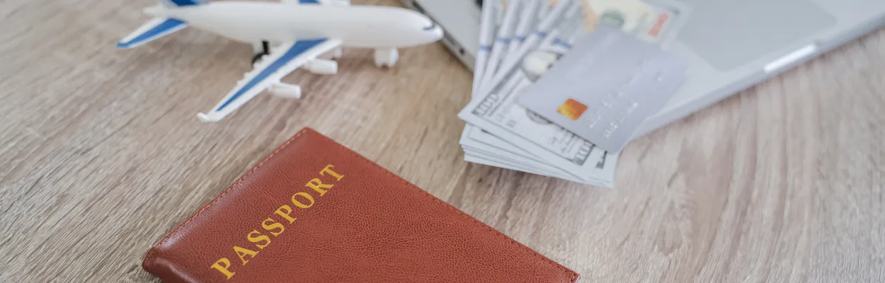 Pieniądze, paszport, samolot i laptop leżące na blacie biurka