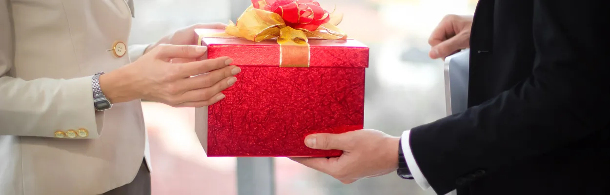 Mężczyzna wręczający kobiecie czerwone pudełko prezentowe z kokardą