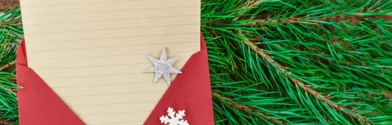 Koperta z papierem w linie ozdobiona gwiazdką i płatkiem śniegu leżąca na świerku