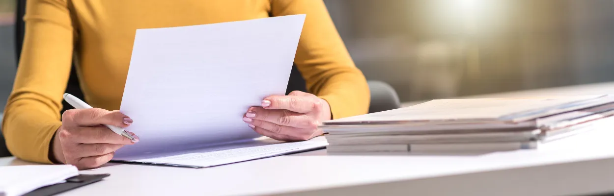 Kobieta siedząca za biurkiem i trzymająca w dłoni kartkę papieru A4