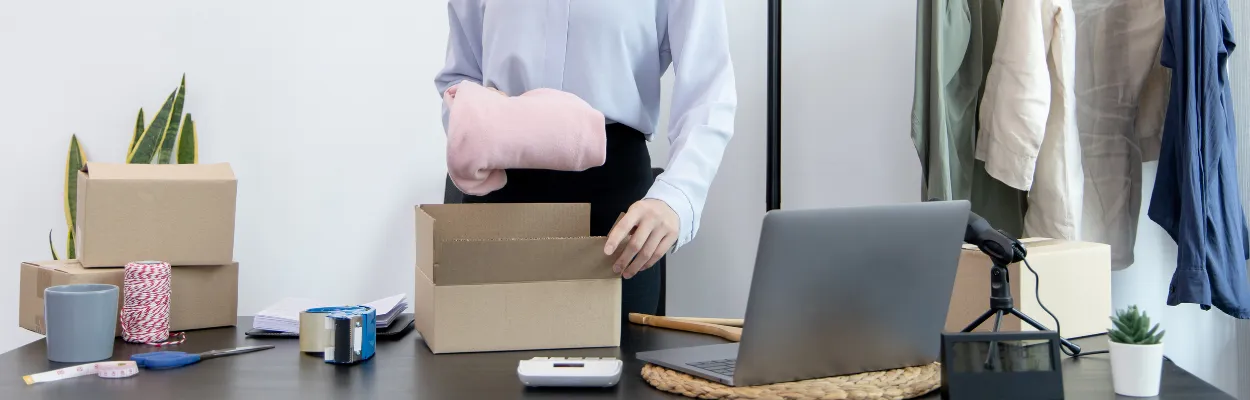 Wkładanie różowej bluzki do kartonu leżącego na biurku