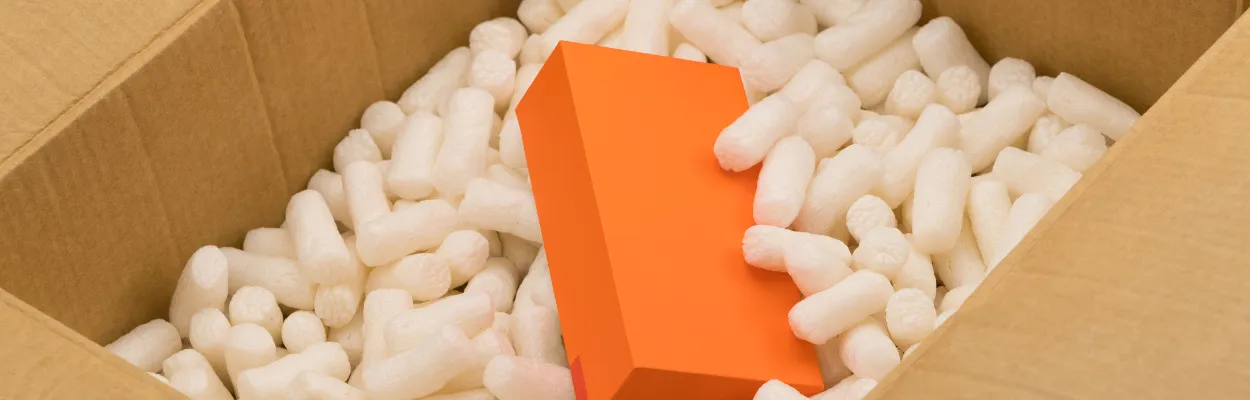Karton wypełniony skropakiem w którym ukryte zostało pomarańczowe pudełko 