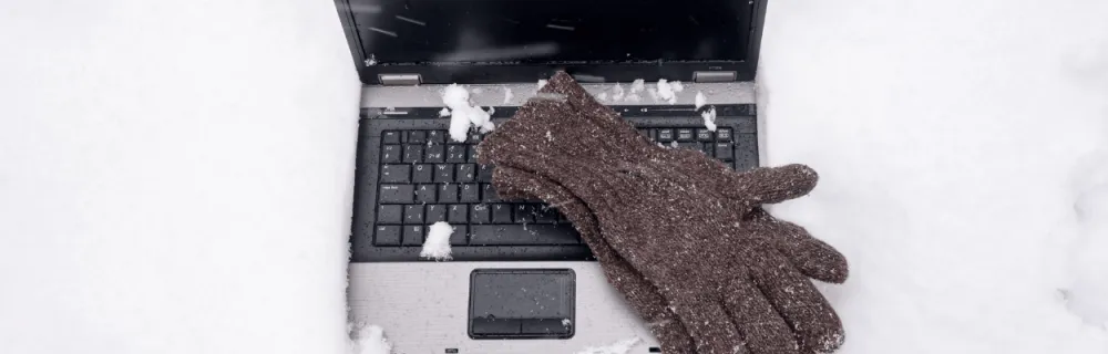 Laptop leżący na śniegu a na nim ułożone rękawiczki